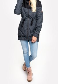 Czarna i szara paskowana kurtka z zamkiem błyskawicznym, regulowanym ściągaczem w talii i czarnymi akcentami. Połączona z jasnoniebieskimi dżinsami i różowymi botkami.