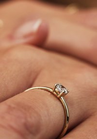 Goldring mit einem runden Diamantbesatz. Das glatte Band zeigt ein poliertes Finish, während der Diamant von vier Prongs gehalten wird.
