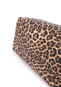 Parte inferior de un bolso con estampado de leopardo y dos tachuelas de metal dorado sobre un fondo blanco.