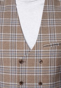 Brązowa kamizelka w kratę z podwójnym zapięciem, z niebieskimi i białymi akcentami, wyposażona w dwa guziki i małą kieszonkę. Pod spodem biała koszula.