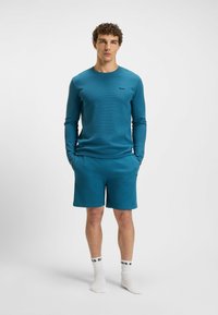 Teal lange mouwen shirt en bijpassende shorts van textuurstof. Bevat een klein merkembleem op de borst en aan de zijkant van de shorts.