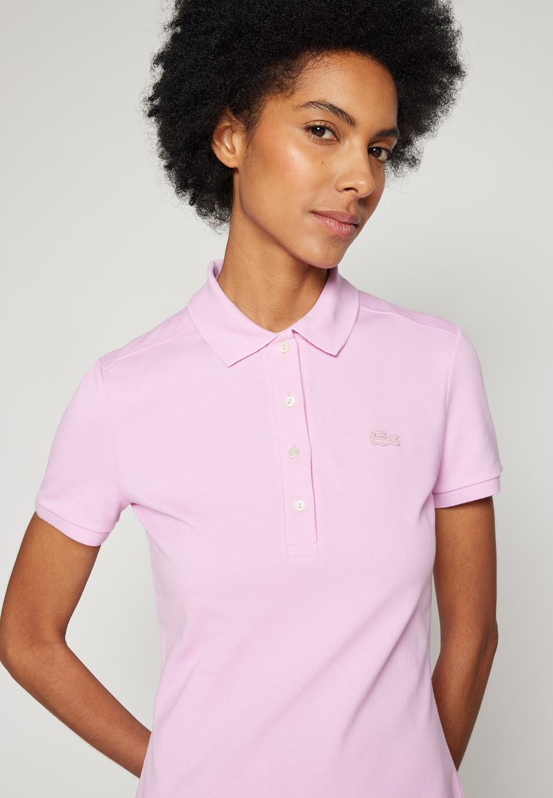 Camisa polo rosa de algodón con cuello clásico y tapeta de cinco botones. Presenta un logo bordado en el área del pecho y mangas cortas.