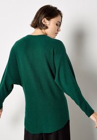 Zielony dzianinowy sweter z d�ługimi, oversize'owymi rękawami, okrągłym dekoltem i lekko zaokrąglonym dołem. Gładka struktura z luźnym krojem.