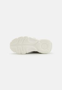 Semelle en caoutchouc blanche avec un motif de texture et des lignes courbes, présentant un bout arrondi et un design de talon de soutien.