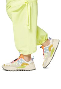 Multicolored sneakers with a mix of cream, yellow, pastel blue, and orange accents. Textured sole and laces in pink. Worn with bright yellow pants.