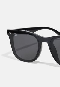 Ochelari de soare negri din plastic, cu lentile întunecate, formă pătrată și un mic accent metalic pe ramă. Prezintă un logo Ray-Ban pe lentila din colțul stâng sus.