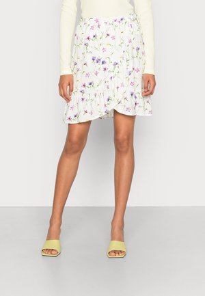 Blomstret omslagsnederdel i hvid med lilla og grønne mønstre, med flæsekant og elastik i taljen. Kombineret med gule slip-in sandaler.