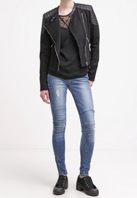 Sort jakke med lynlås foran og ribbede skulderdetaljer, lagd over en sort top. Båret med slidte blå skinny jeans og sorte platform-sko.