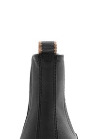 Botín de cuero negro hasta el tobillo con acabado texturizado, que presenta una lengüeta trenzada con un patrón a rayas en la parte superior.