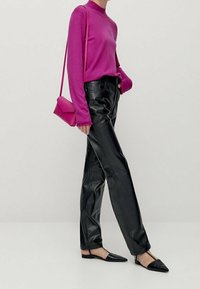 Vrouw in een felroze lang mouwtop, zwarte leren broek, zwarte puntige ballerina's en een bijpassende roze schoudertas.