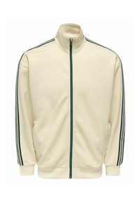 Veste de sport couleur crème avec une fermeture éclair vert foncé et trois bandes vert foncé courant le long des manches, de l'épaule jusqu'au poignet.