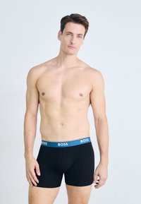 Black boxer briefs with a blue waistband featuring "BOSS" logo; smooth texture, fitted design, and mid-thigh length.