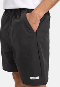 Schwarze Shorts aus leichtem Stoff, mit einem elastischen Bund, Seitentaschen und einem kleinen Logo-Tag am Saum.