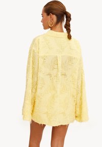 Gele gestructureerde oversized shirt met rafelige details, lange mouwen en een rechte zoom. Ontworpen met een relaxte pasvorm en een kraag.
