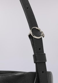 Svart läderväska strap med slät yta, utrustad med en silverfärgad metallspänne och justerbar längd med stansade hål för anpassning.