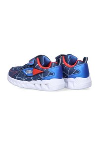 Zapatillas deportivas azules y rojas con un upper de tela texturizada, que presenta un patrón de telaraña, una correa de Velcro y una suela blanca con detalles.