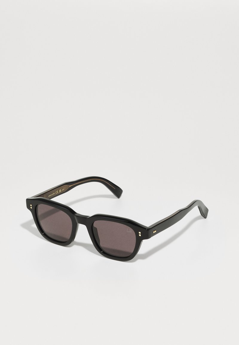 Black sunglasses with a squared frame, dark lenses, and gold accents on the temples. Made from plastic with a matte finish.