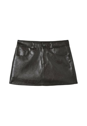 Jeune femme portant un pull rayé épaules dénudées, une mini-jupe en cuir noire et des bottes noires montantes cloutées, debout devant un fond olive.
