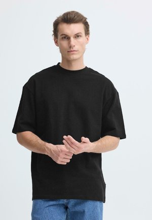 Schwarzes übergroßes T-Shirt aus Baumwolle mit kurzen Ärmeln und rundem Ausschnitt. Verfügt über einen Seitennaht-Akzent und eine lockere Passform.