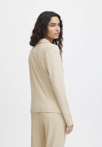 Beige skräddarsydd kavaj med ett subtilt randigt m�önster, med slagkrage och långa ärmar. Texturerat tyg med en figurnära passform.