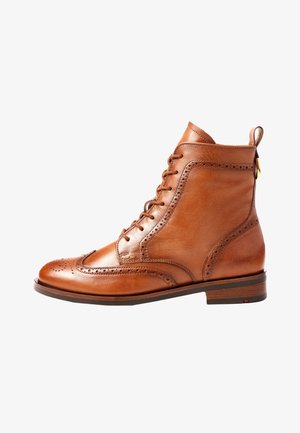 Bottine brogue en cuir marron avec lacets, perforations à bout d'aile, languette de tirage et petit talon en bois sur fond blanc.