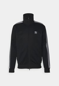 Svart zip-up sportjacka i polyester med hög krage, med vita tre-rands accenter på axlarna och liten Adidas-logotyp på bröstet.