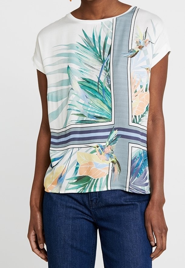 Blusa blanca de manga corta con rayas azules, hojas tropicales verdes y durazno, y estampados de colibríes coloridos, combinada con jeans azul oscuro.