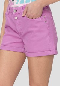 Shorts en denim rose avec une coupe classique, présentant des ourlets retroussés, deux poches avant et des détails en métal brillant sur les boutons.