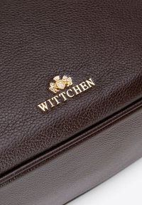 Portafoglio in pelle marrone con texture, dotato di un logo dorato impresso "WITTCHEN" e un emblema decorativo, che presenta una superficie liscia e dettagli raffinati.