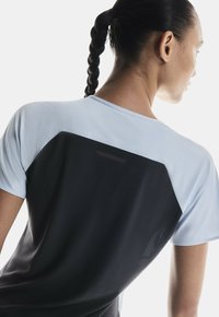 T-shirt de sport bleu clair et noir avec un panneau en mesh au dos, des manches courtes et une texture lisse avec une coupe moderne.