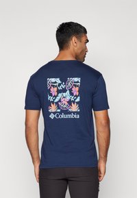 Mørkeblå t-skjorte med korte ermer som har et fargerikt blomsterdesign på ryggen, med Columbia-logoen under designet.