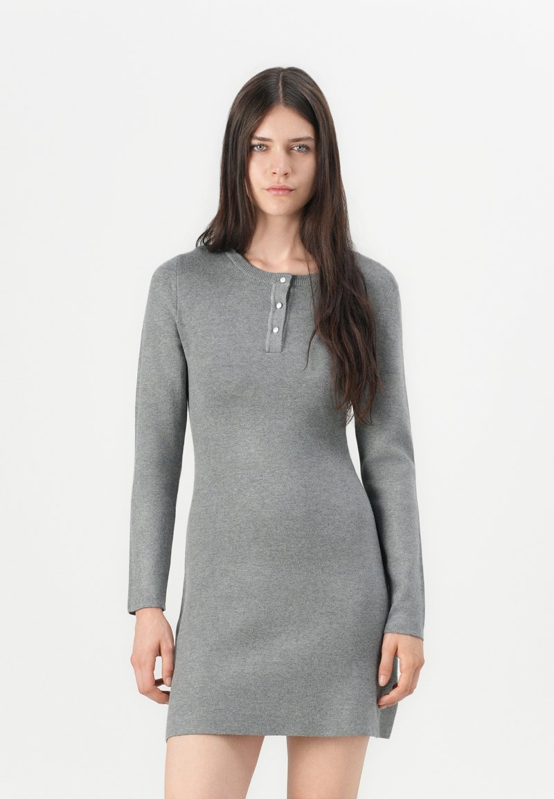 Robe en tricot grise à manches longues, col rond, et patte de boutonnage avec trois boutons au niveau du col. Texture lisse, design ajusté.