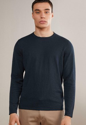 Navyblauwe blouse met lange mouwen, gemaakt van een gestructureerde stof, met een ronde halslijn en een relaxte pasvorm, gecombineerd met lichtbeige broek.