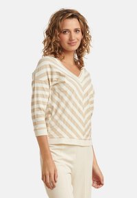 Beige und creme gestreifter Pullover mit V-Ausschnitt, dreiviertel �Ärmeln und geripptem Saum. Weicher Stoff, Zickzackmuster.