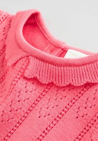 Rózsaszín kötött pulóver, fodros gallérral, textúrált mintákkal és bordázott részletekkel. Puha fonal nyitott mintázattal.