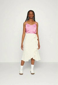 Camisola de cetim rosa, saia envolvente branca com padrão floral e detalhe de babados, combinada com ténis brancos e meias até ao tornozelo.