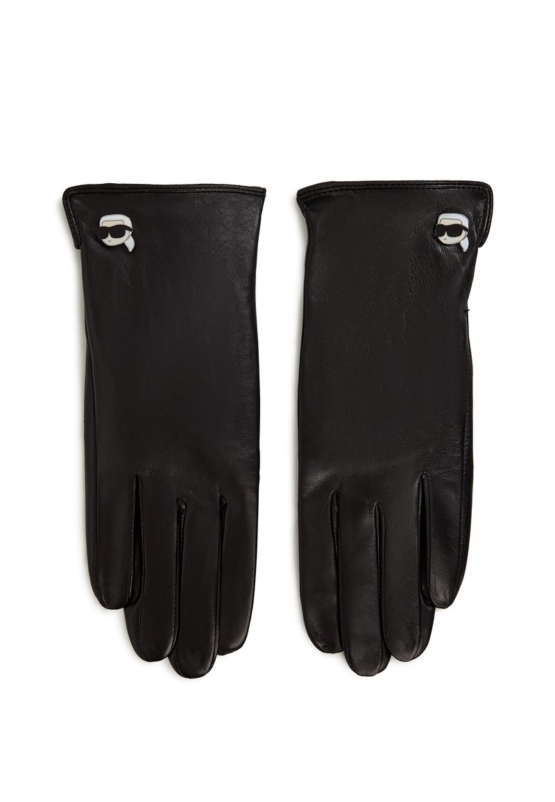 Ett par svarta läderhandskar med små vit- och svartaxelstyled ansiktsnålar nära handleden, liggande platt på vit bakgrund.