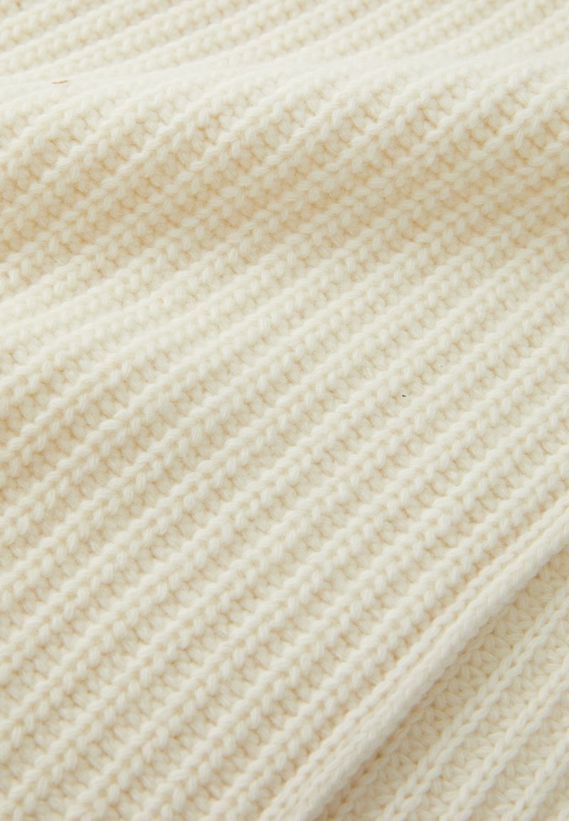 Flauschiger, cremefarbener Strickstoff mit einem strukturierten Rippenmuster, das weiche, dicke Garne für Wärme und Komfort bietet.