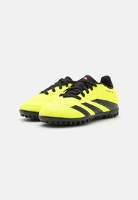 Zapatillas de fútbol sintéticas amarillas con acentos en negro, que cuentan con una parte superior texturizada, cierre de cordones y suela de goma para mayor tracción.