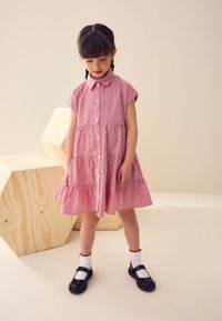 Vestito a quadretti rossi e bianchi con maniche corte e chiusura con bottoni, caratterizzato da una gonna a balze. Abbinato a scarpe Mary Jane nere e calzini bianchi.