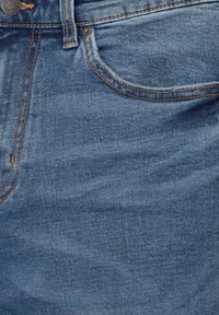 Jean en denim bleu en gros plan montrant la poche avant, la boucle de ceinture, le bouton métallique et le détail de couture orange contrastée.