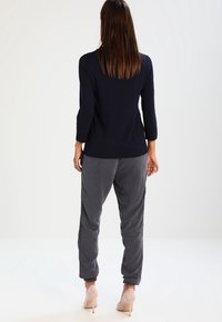 Merimiesmallinen neule, jossa on kolme neljäsosahihaa, yhdistetty harmaisiin juoksuhousuihin, joissa on sivuraitoja ja kapeutetut resorit. Kevyet korot viimeistelevät asun.