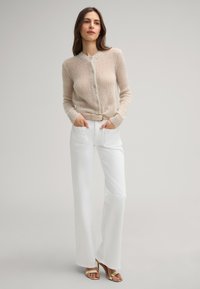Beige Strickjacke mit Rundhalsausschnitt und Knopfverschluss, kombiniert mit weißen weit geschnittenen Hosen und einem beigen Gürtel, dazu Riemchen-Heels.