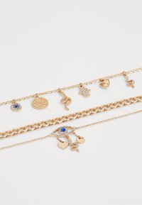 Gold-tone layered bracelets featuring various charms, including a sparkling eye, hearts, and a snake, decorated with blue and clear stones.
