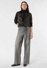 Czarna satynowa koszula zapinana na guziki z podwiniętymi rękawami, zestawiona z szarymi szerokimi dżinsami z wysokim stanem, ozdobionymi czarnym paskiem do wiązania, oraz czarnymi botkami za kostkę.