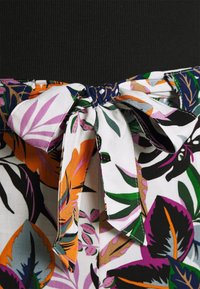 Ceinture en tissu nouée à l'avant, avec un motif coloré de feuilles tropicales en orange, violet, vert et noir sur fond blanc.