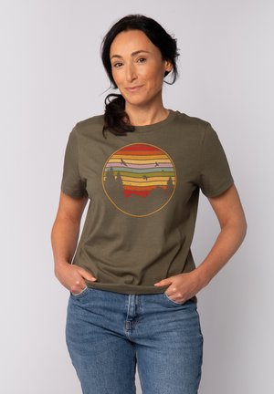Olijfgroene katoenen t-shirt met een cirkelvormige grafiek met horizontale strepen in oranje, roze en geel, die silhouetten van bomen en vogels weergeeft.