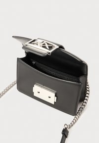 Black leather handbag with a silver geometric closure, chain strap, and an open interior revealing a zipper compartment.