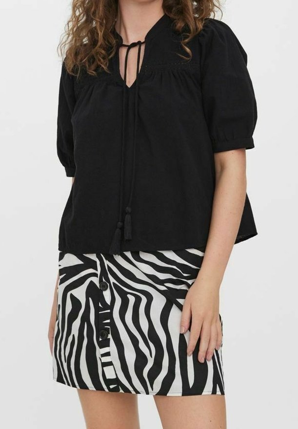 Top nero con maniche a sbuffo, dotato di scollatura con lacci e cuciture decorative, abbinato a una gonna bianca e nera a strisce zebra con bottoni.