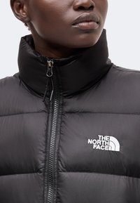 Άτομο που φοράει μαύρο μπουφάν The North Face με ψηλό γιακά και εμφανή φερμουάρ στο κέντρο.